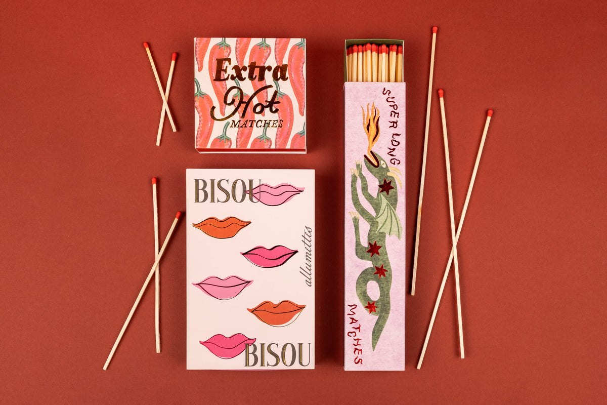 Dragon - Extra Long Boxed Matches include two rectangular matchboxes, one with chili peppers labeled Extra Hot Matches and one with pink lips, plus a tall sliding box decorated with a dragon breathing fire, surrounded by loose, extra long matches.