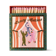 Dancing Jesters - Square Boxed Matches features three pajama-clad dancers on stage with pink curtains and gold accents; a whimsical gift containing pink-tipped safety matches.