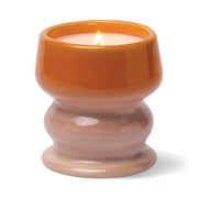 A lit Infrared Mango - Melt 8.5 oz Candle, presented in a glossy, hand-glazed ceramic vessel featuring an orange upper section and a light pinkish base, emits a tropical fragrance and is photographed on a white background.