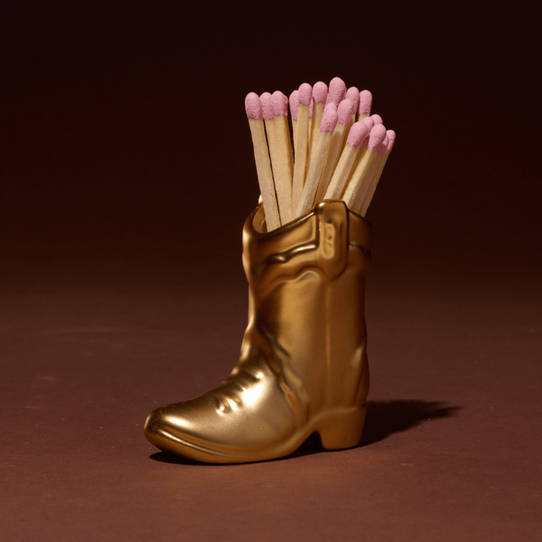 Gold boot-shaped matchbox with pink matches on a brown background