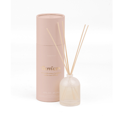 The Flowers - 1.5 oz Diffuser features a pink giftable tube and a milky glass bottle with pale liquid and wooden reeds, both showcasing a minimalist, elegant design.