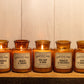 5 of the Apothecary candle line, including Amber & Smoke, on a wooden shelf.  All lit.