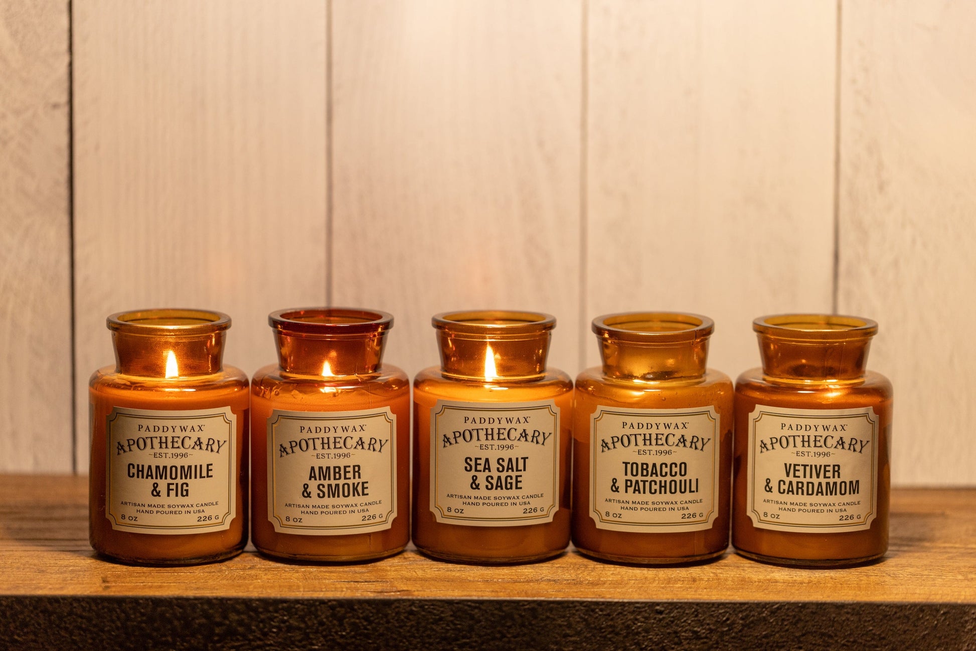 5 of the Apothecary candle line, including Amber & Smoke, on a wooden shelf.  All lit.