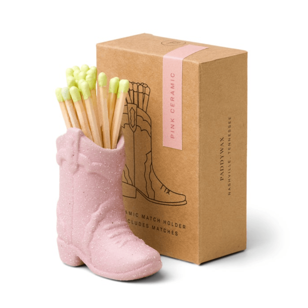 small pink ceramic cowboy boot pictured holding green-tipped matches in front of the brown packaging