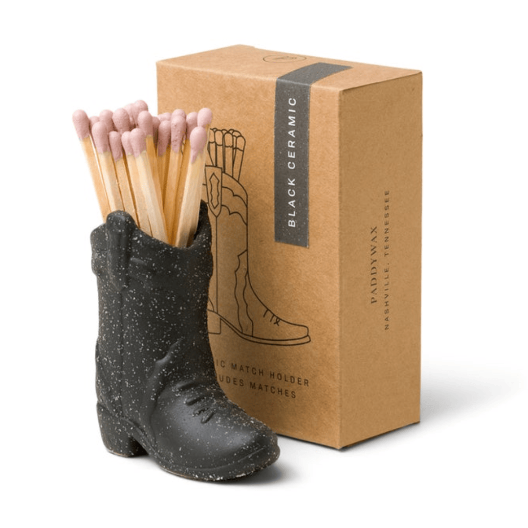 small black ceramic cowboy boot pictured holding pink-tipped matches in front of the brown packaging