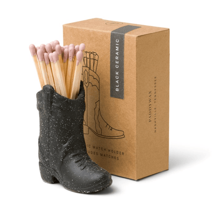small black ceramic cowboy boot pictured holding pink-tipped matches in front of the brown packaging