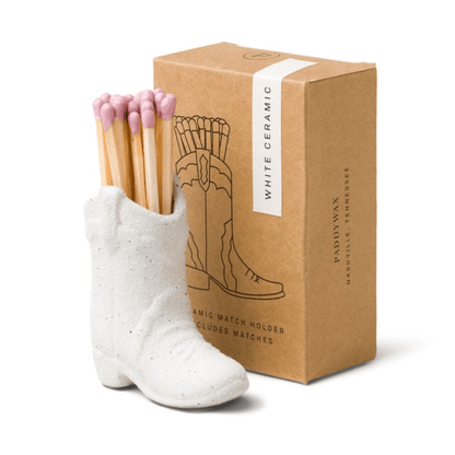 White ceramic boot match holder with matches and a brown packaging box on a white background
