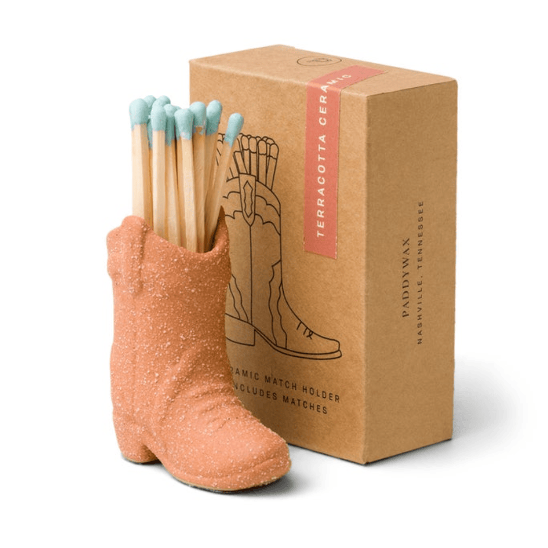 terracotta (desert orange) ceramic cowboy boot pictured holding blue-tipped matches in front of the brown packaging