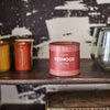 A Redwood - Parks 6 oz Tin Candle rests on a wooden shelf next to ceramic cups and glasses, above a UTOPIA box—an ideal outdoor gift for nature lovers.