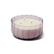 The Salted Iris - 12 oz Candle features three wicks ablaze in a round, translucent ribbed glass container, viewed at an angle against a white background.