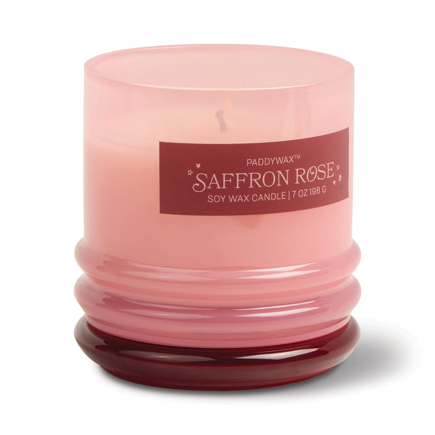 A pink glass candle jar with a red base and a label reading "Saffron Rose - Stack 7 oz Candle." This rose petal-scented candle features light pink wax in a reusable glass container for extra charm.