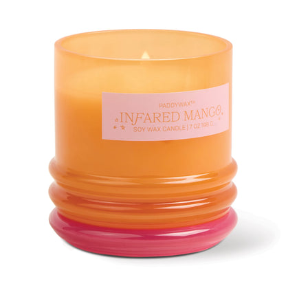 An orange glass vessel with a pink base holds the lit Infrared Mango - Stack 7 oz Candle. The label reads Paddywax, Soy Wax Candle, 7 oz/198 g. Once finished, repurpose the vessel for stylish storage.