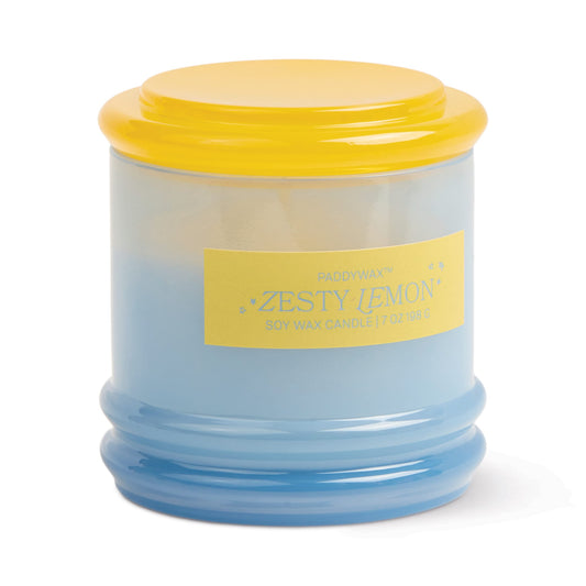 A light blue reusable glass jar candle with a rounded, ribbed base and bright yellow lid. The front label reads “Zesty Lemon - Stack 7 oz Candle,” emphasizing its citrus scent and refreshing aroma.