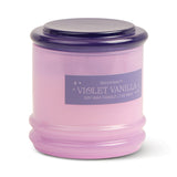 A lavender glass vessel with a dark purple lid, labeled Violet Vanilla - Stack 7 oz Candle, offers a floral scent and reusable style to add elegance to any room.