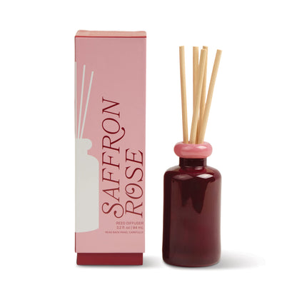 A pink and red box labeled "Saffron Rose - Stack 3.2 oz Diffuser" stands beside a matching dark red glass diffuser with a pink cap and natural wooden reeds, ideal for adding continuous fragrance to modern decor.