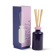 A violet glass 3.2 oz Violet Vanilla diffuser with wooden reeds stands by a matching box labeled "Violet Vanilla" in bold purple, featuring a minimalist diffuser illustration.