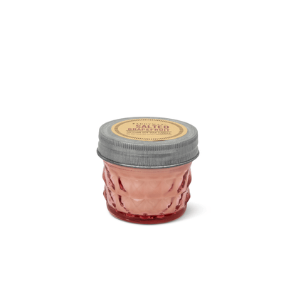 A small glass jar candle with a textured pink body, a silver metal lid, and a round beige label reading 'SALTED' and 'Bergamot Scented Candle'.