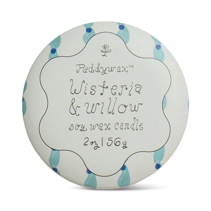 A round candle tin lid with a white background, adorned with blue and teal leaves. The text reads: Wisteria & Willow - Tulip 2 oz Tin Candle, evoking fresh spring mornings, in a decorative font.