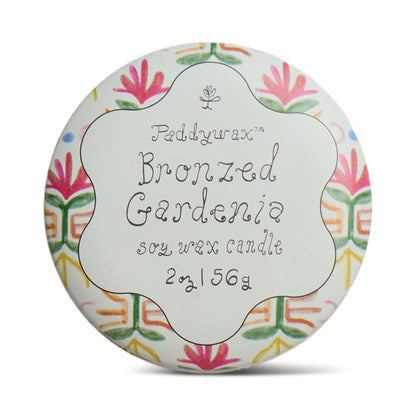Bronzed Gardenia - Tulip 2 oz Tin Candle: Soy wax with creamy florals and sunlit citrus notes. Round tin features a white background, colorful floral patterns on the edge, and handwritten-style text in the center.