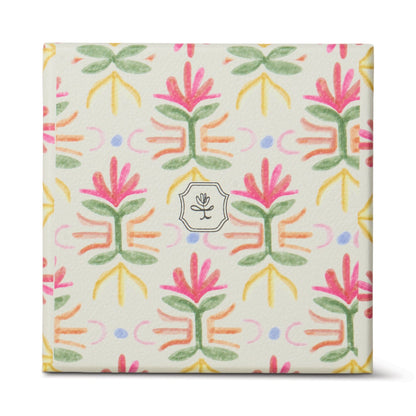 The Bronzed Gardenia - Tulip 5.5 oz Candle comes in a square box with a colorful floral pattern in pink, green, yellow, and purple on white, featuring a small circular flower logo—perfect for adding floral charm to your home décor.
