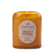 A lit Tobacco + Patchouli - Vista 5 oz Candle adds modern home decor style and a luxurious scent against a clean white background.