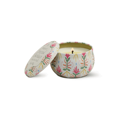 The Bronzed Gardenia - Tulip 2 oz Tin Candle glows in a round tin with a colorful leaf design, its lid set aside, releasing creamy florals and bronzed gardenia for an elegant touch.