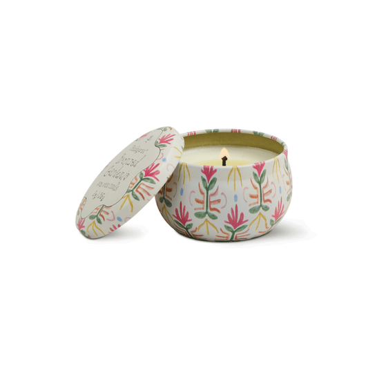 The Bronzed Gardenia - Tulip 2 oz Tin Candle glows in a round tin with a colorful leaf design, its lid set aside, releasing creamy florals and bronzed gardenia for an elegant touch.