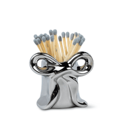The Metallic Bow Match Holder features a shiny silver, abstract twisted design and comes filled with 25 upright safety matches tipped in gray.