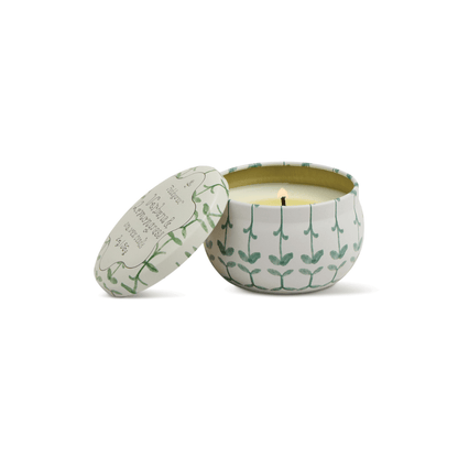 The Verbena & Lemongrass - Tulip 2 oz Tin Candle sits in a white round tin with green leaf patterns and a matching lid with text, evoking a fresh herb garden against a plain white background.
