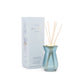 4 oz. blue glass diffuser with a brushed gold metal plate; pictured with bamboo sticks inside, in front of the powder blue package