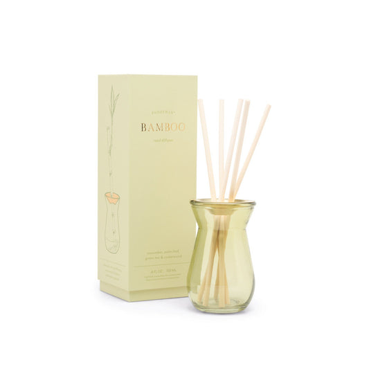 4 oz. sage green glass diffuser with a brushed gold metal plate; pictured with bamboo sticks inside, in front of the sage green package