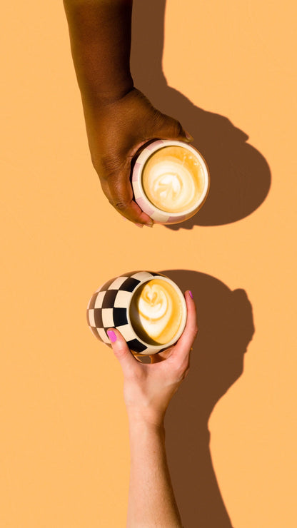 Two hands holding Checkmate candles repurposed as coffee mugs. 