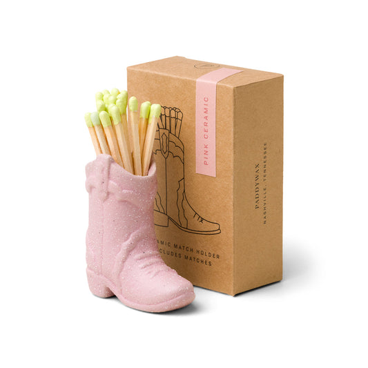 small pink ceramic cowboy boot pictured holding green-tipped matches in front of the brown packaging