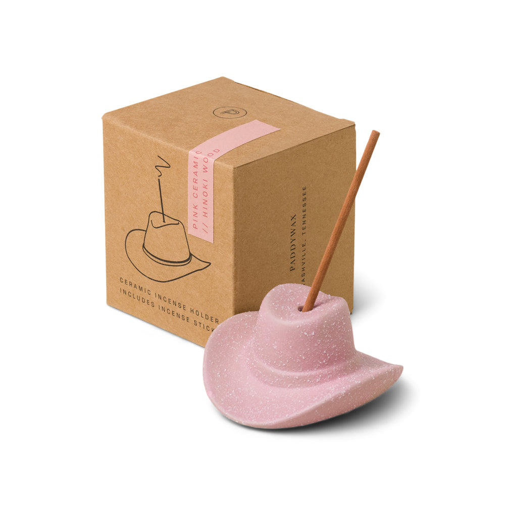 Pink ceramic cowboy hat holding incense stick in the top; pictured in front of brown packaging