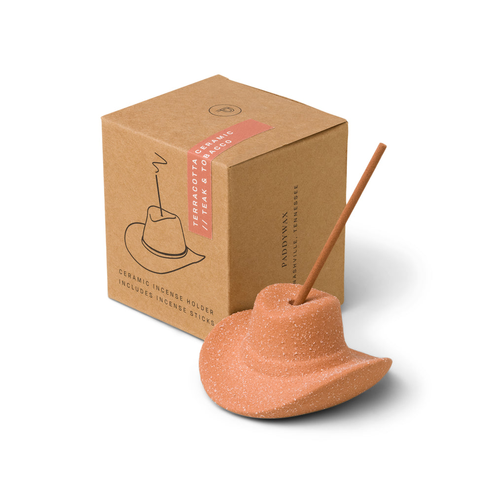 Terracotta (desert orange) ceramic cowboy hat holding incense stick in the top; pictured in front of brown packaging