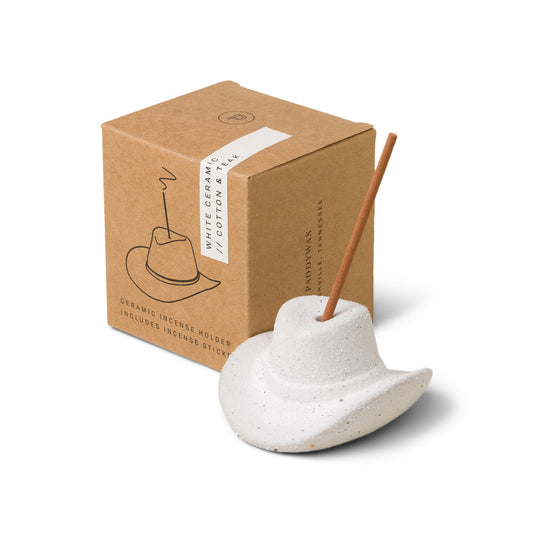 White ceramic cowboy hat holding incense stick in the top; pictured in front of brown packaging