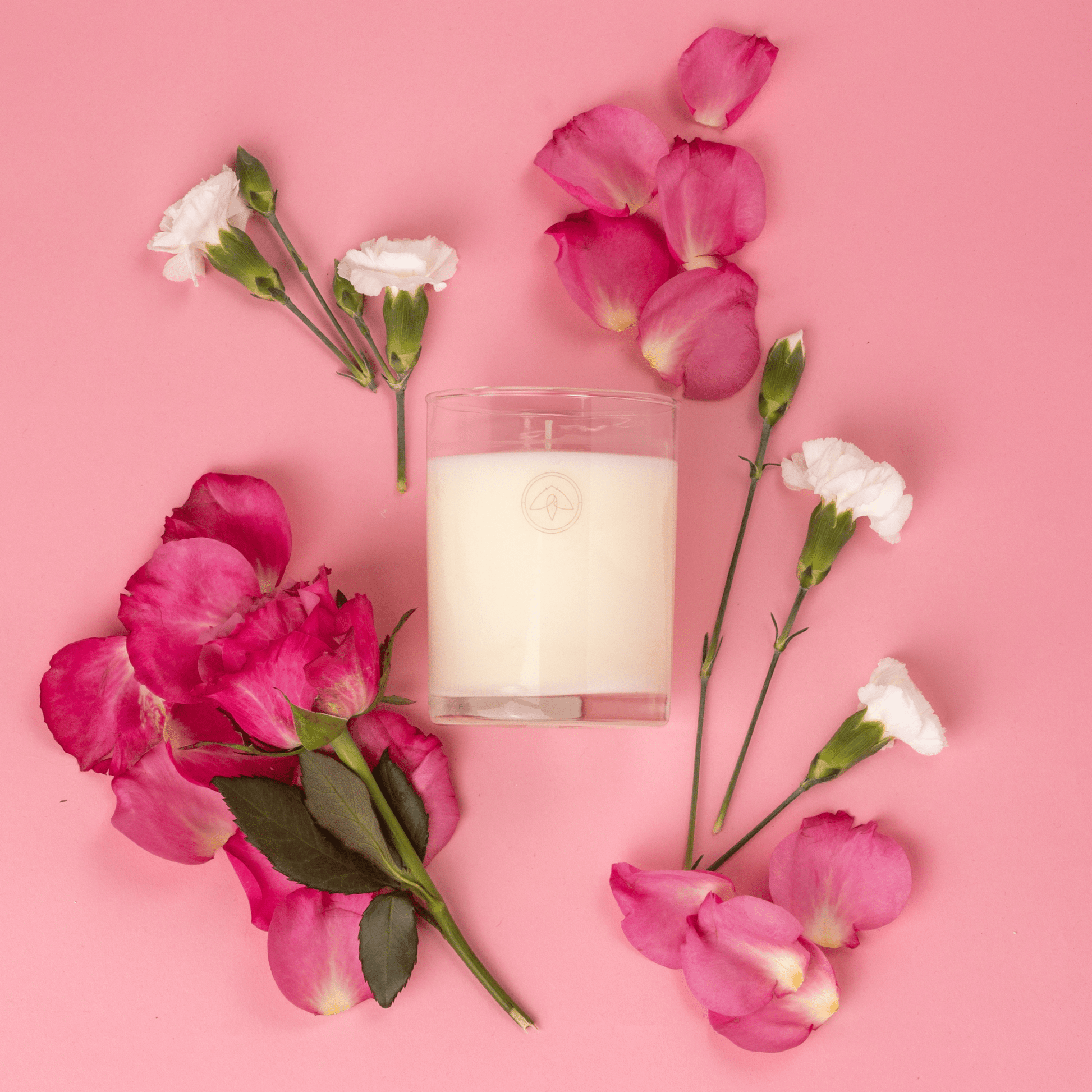 Clarity Peony candle on a pink background surrounded by flowers and flower petals