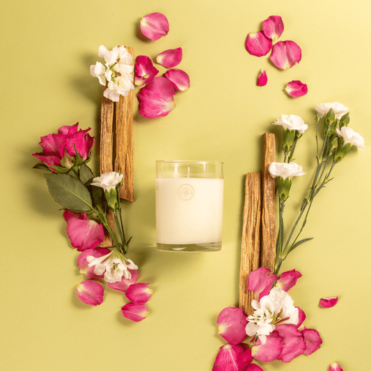 Clarity Sweet Magnolia candle on a greenish background surrounded by cedarwood and white and pink flowers