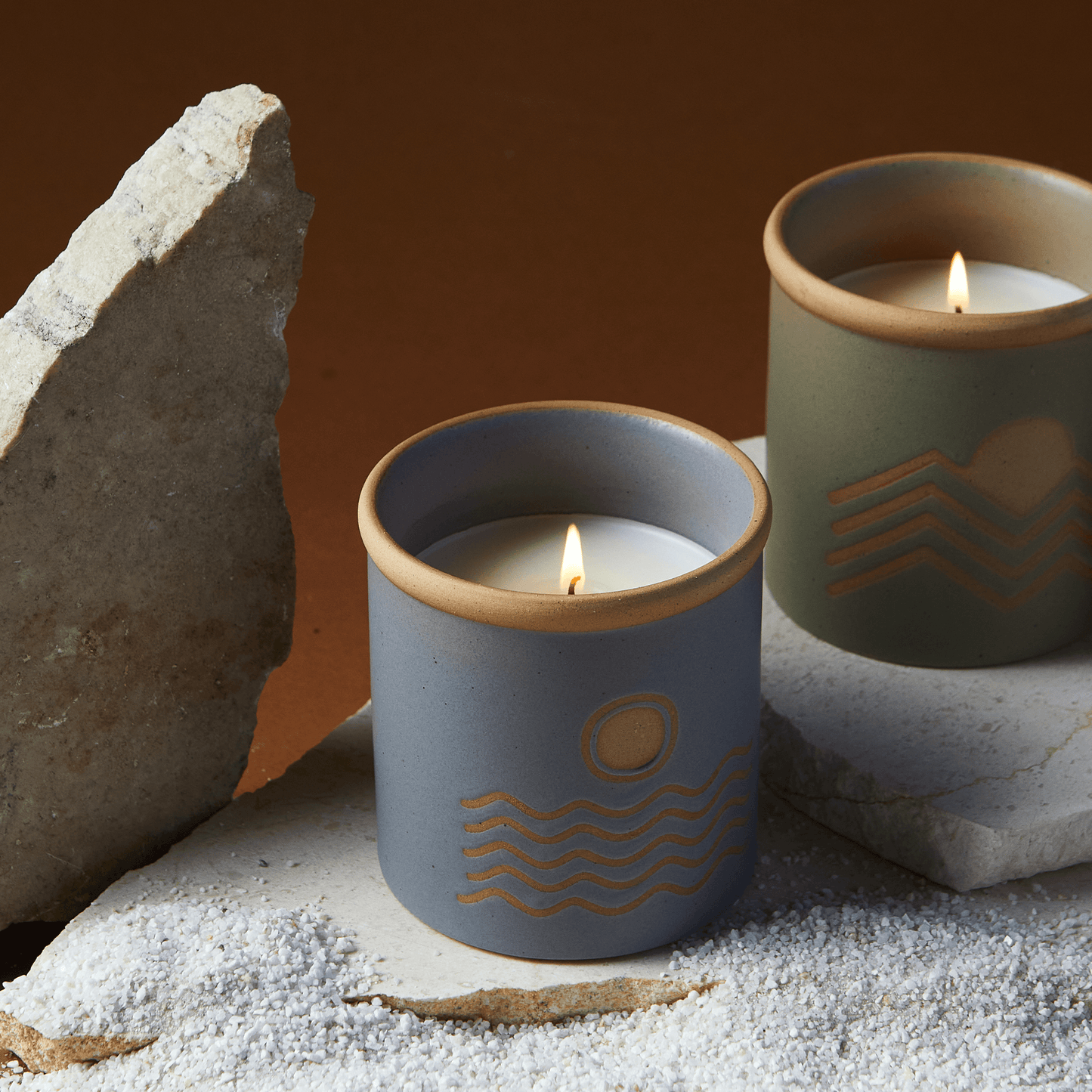  8 oz blue ceramic vessel with ocean design and a cork lid (also containing the same design); pictured lit with other candles