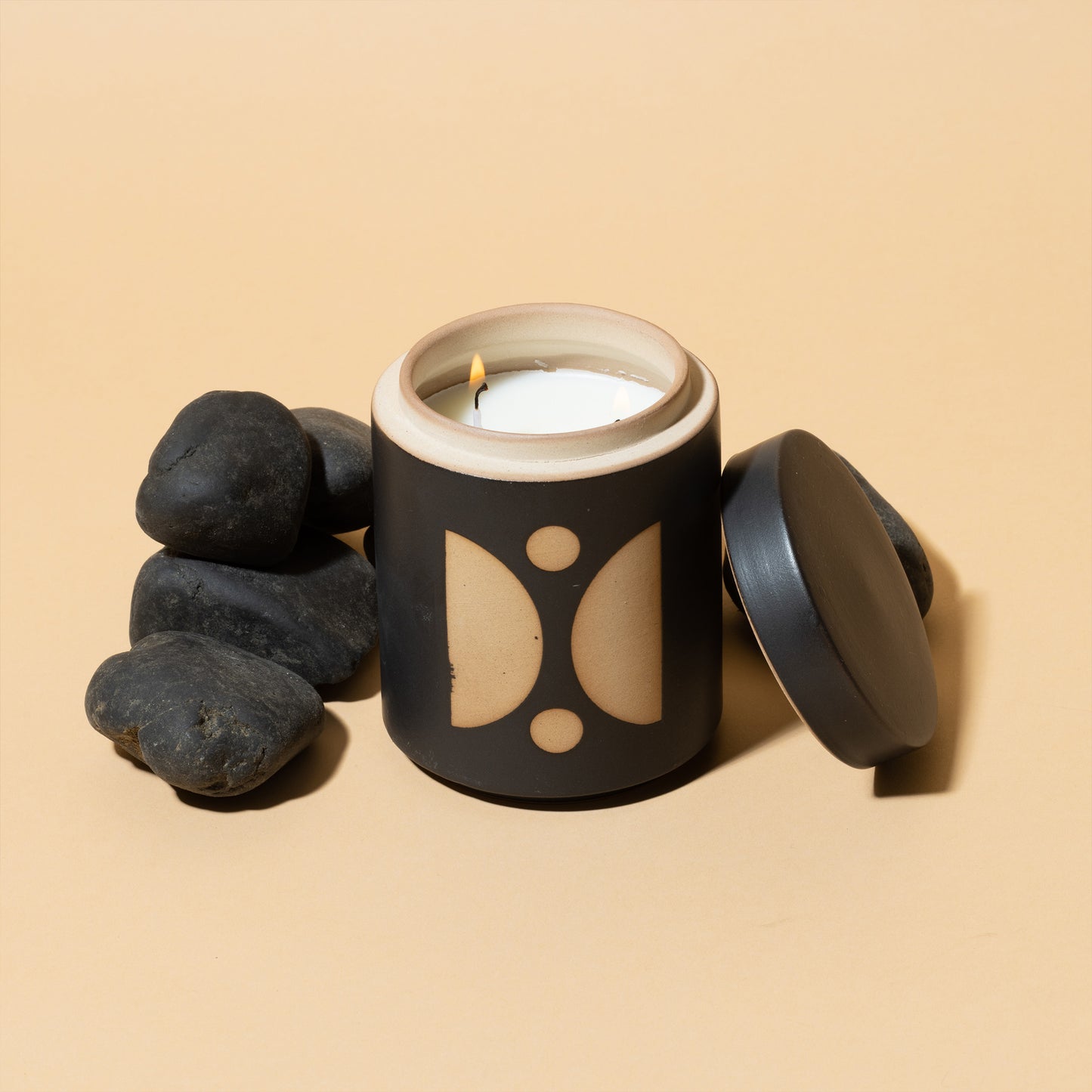 12 oz black cylindrical ceramic vessel with ceramic lid; white wax and two cotton wicks; reflected beige semi-circle design on the side