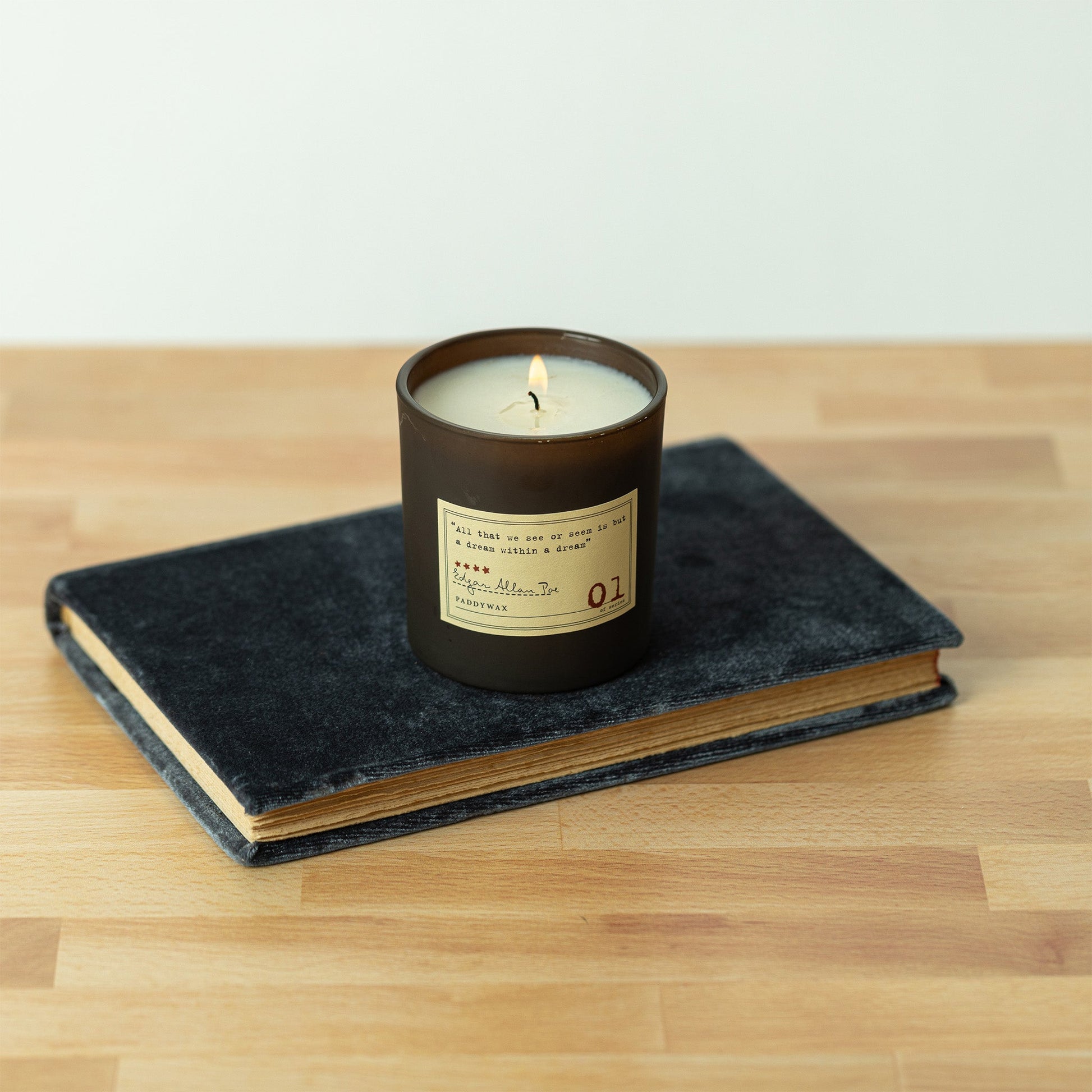 Library Edgar Allan Poe soy wax candle with single wick burning on top of book on hardwood surface