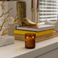 10oz Glow two wick canlde on white table with books, metal boot decor and candlesticks with window in background