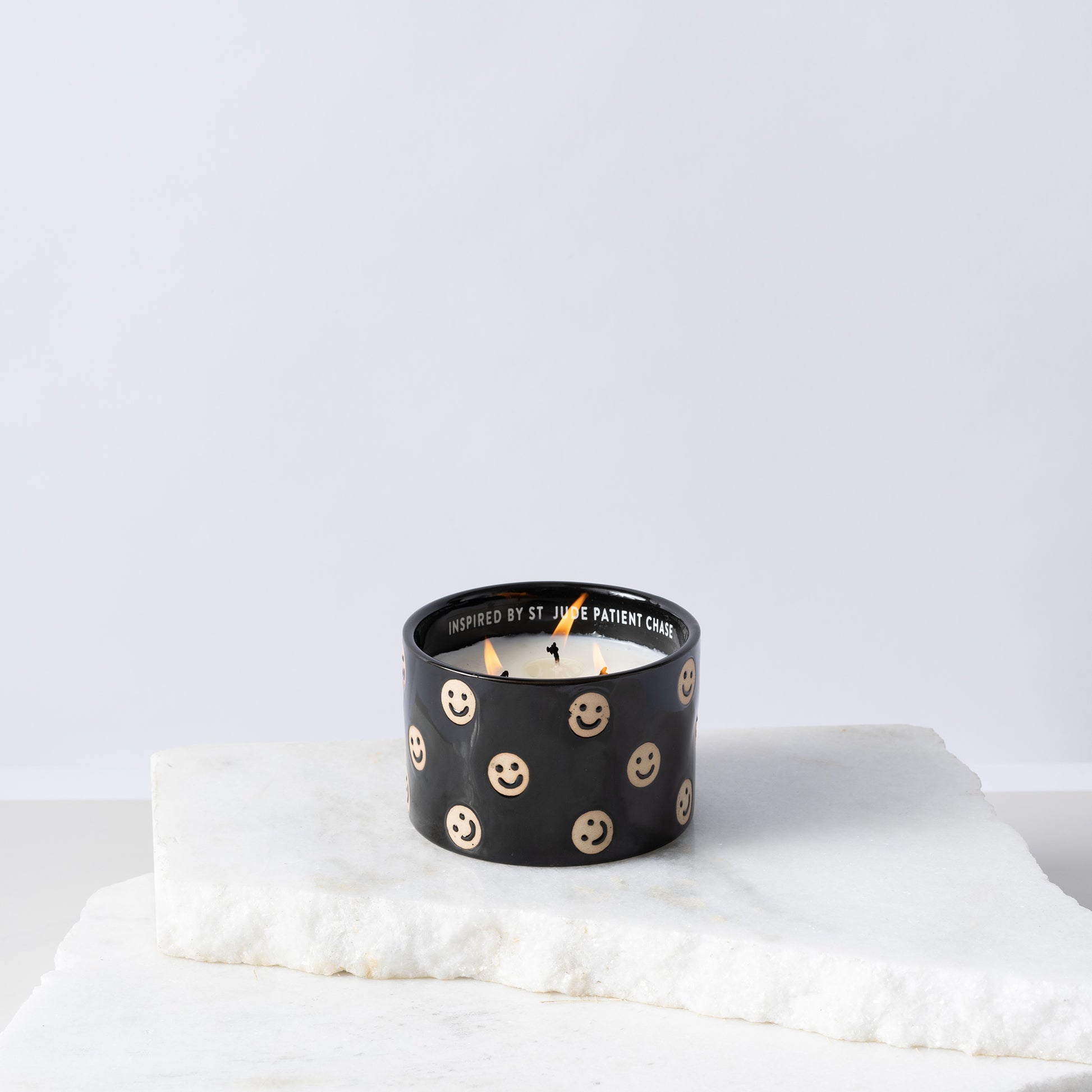 Black ceramic candle with smiley faces and white soy wax center with three wicks burning