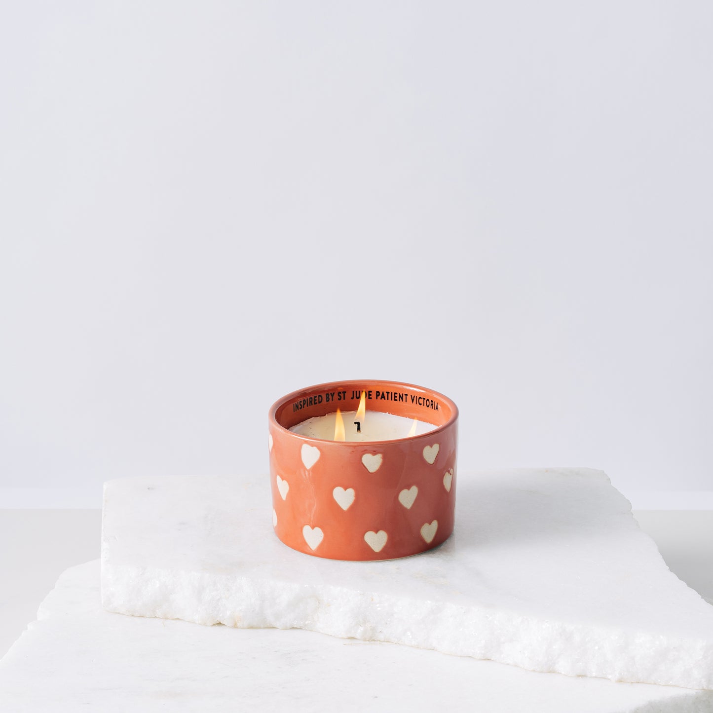 Red ceramic candle with hearts and white soy wax center with three wicks burning 