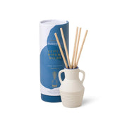 The Santorini 4 fl oz. Diffuser - Cliff & Hinoki Wood sits beside its cylindrical packaging, filling the air with a fresh scent inspired by the Aegean Sea.