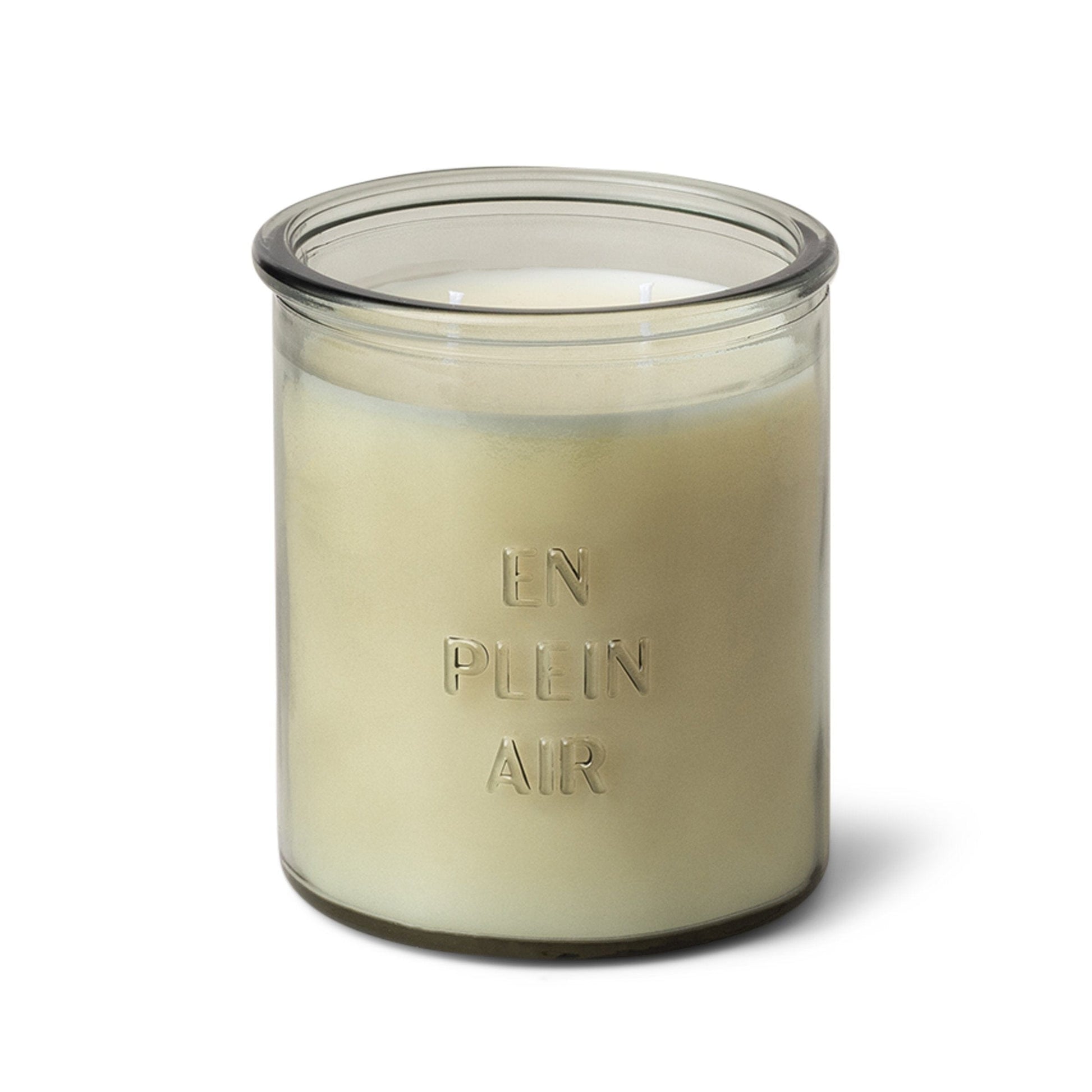 Clear glass candle with "En Plein Air" as raised text on the glass, white soy wax inside, and two cotton wicks on white background