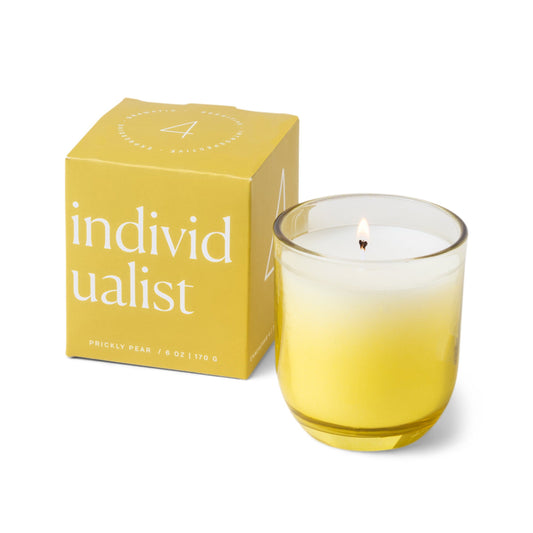 Candle with a vessel of clear glass that fades to yellow at the bottom; pictured next to the yellow box which reads “individualist”