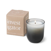 A gray ombre glass Enneagram #5 Investigator 5 oz Candle in eucalyptus santal scent burns beside its beige box, featuring modern minimalist typography—the ideal gift for those who value unique, thoughtful design.